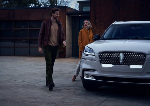 A man and a woman approaching a 2024 Lincoln Aviator® SUV, which illuminates certain lights when they are close | Pinnacle Lincoln in Nicholasville KY