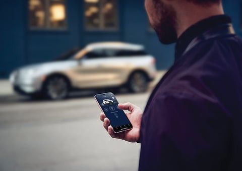 A person is shown interacting with a smartphone to connect to a Lincoln vehicle across the street. | Pinnacle Lincoln in Nicholasville KY